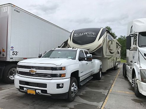 A pickup truck pulling a fifthwheel trailer between two big rigs