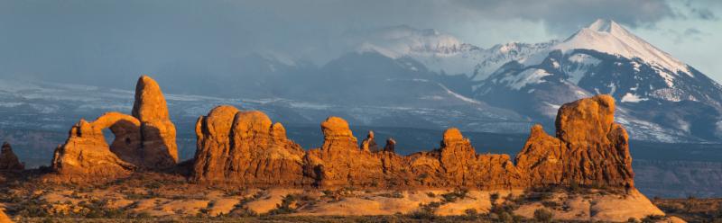 Photo taken at Arches National Park showing red rocks and arches in the foreground and mountains in the background. 