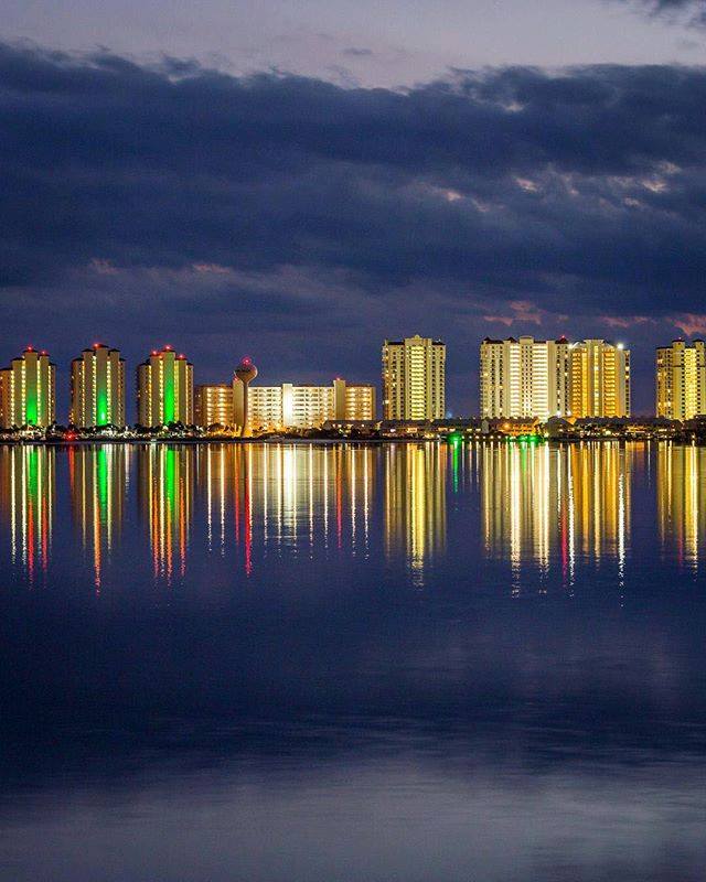 Waterfront condos light up the night sky, reflected in the water.