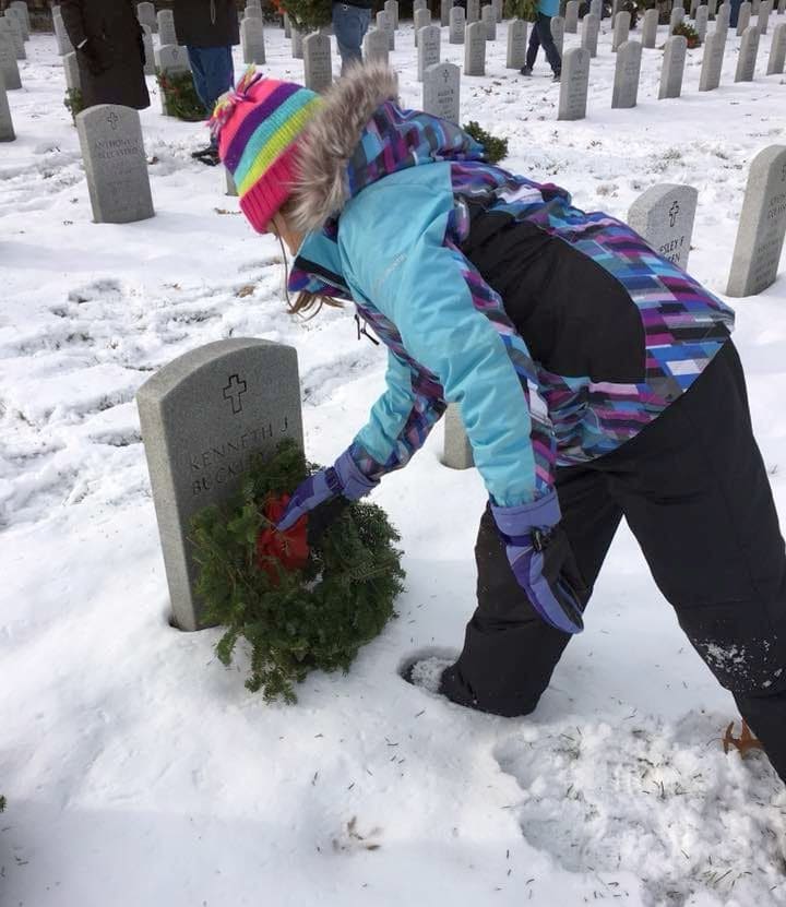Wreaths Across America - girl laying wreath on a soldiers grave
