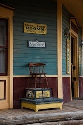 5. Vintage wooden chair placed on a decorative box outside a colorful retro storefront with signs for Rooms, Shoe Shine, and Fun Holes, evoking nostalgic charm and classic Americana.