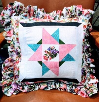 Pink, blue, and green floral quilt with ruffled floral border showcasing intricate quilting craftsmanship. Perfect for home decor or as a handcrafted gift. Vibrant colors and detailed patterns highlight quilting artistry.