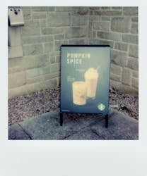Pumpkin Spice Starbucks drink promotional sign outside a coffee shop on a sidewalk.