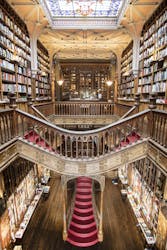 Arts and crafts style library interior with ornate woodwork, grand staircase, and high bookshelves filled with books, showcasing vintage elegance and architectural beauty.