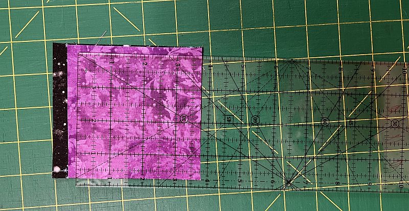 Acrylic quilting ruler and transparent square ruler on a green cutting mat with measurement grid for precise fabric cutting.