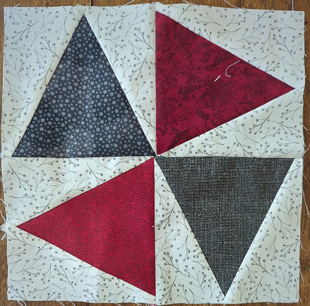 Bright quilt block featuring bold red, black, and navy blue triangles on a light, leaf-printed background, perfect for handmade quilt projects and sewing crafts.