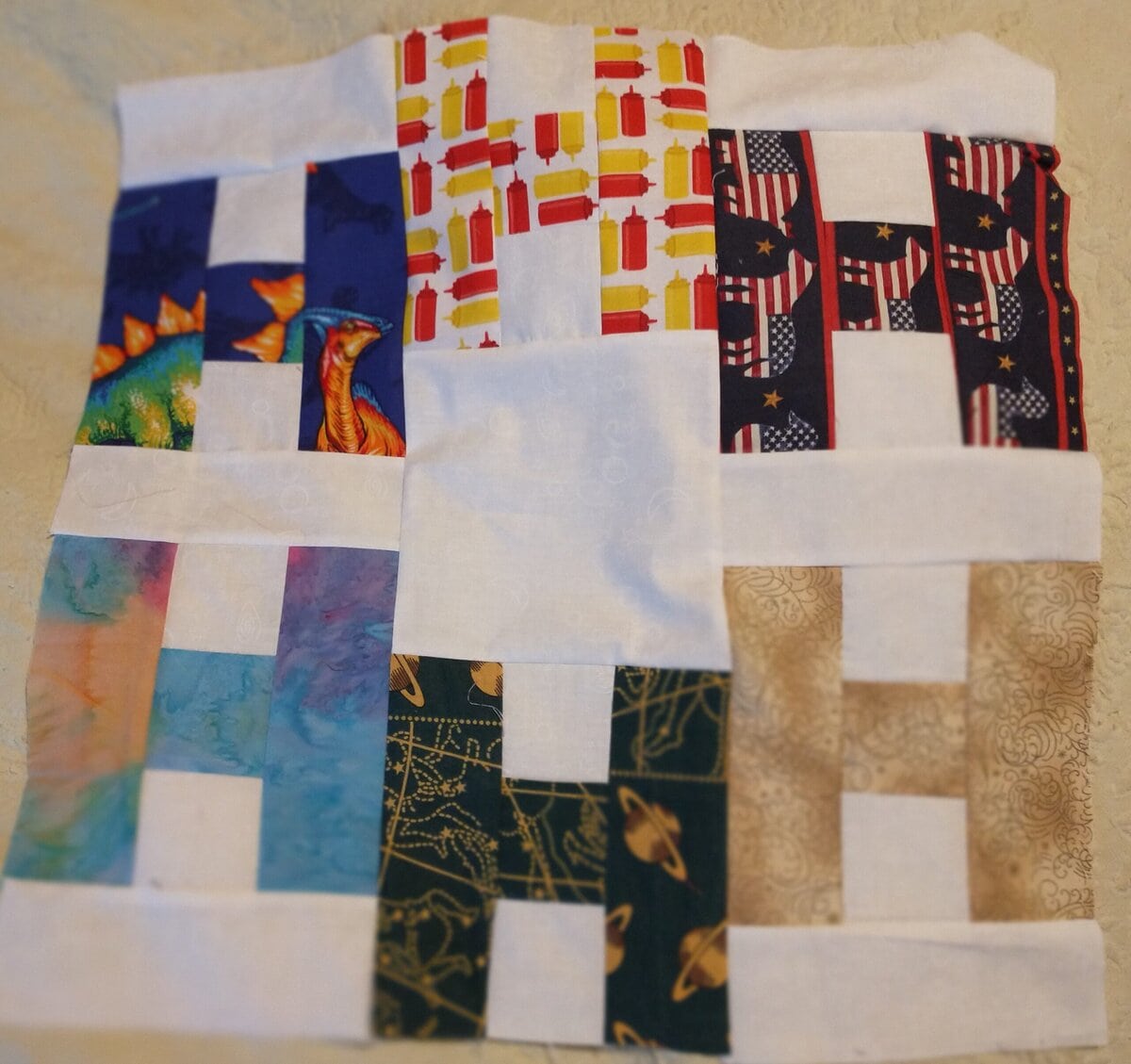 Hello-Carole-H block A quilt block made from nine smaller squares, each featuring different colorful patterns, including dinosaurs, books, American flags, abstract prints, and gold swirls, bordered with white sashing.