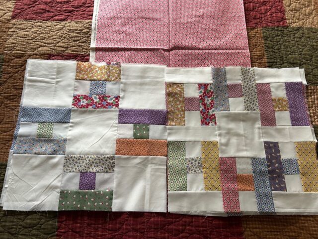 Hello-Marylyn-blocks Several quilt blocks featuring colorful, patterned fabric strips sewn together with white fabric are displayed on top of a red and pink patterned cloth and a larger quilted background.