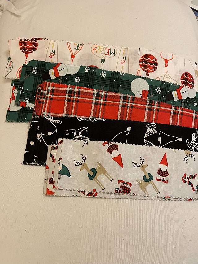 Hello-Mercedes-fabric Five rectangular pieces of fabric with Christmas-themed patterns, including snowmen, plaid, reindeer, and festive decorations, are arranged in a fan shape on a white surface.
