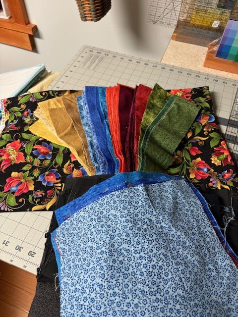 A selection of colorful fabric pieces—including floral, solid, and blue patterned fabrics—arranged on a cutting mat in a sewing workspace.