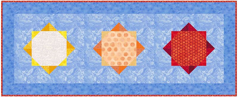 Sunny-Days-Table-Runner A rectangular quilted table runner with a blue floral background, featuring three geometric sun designs: yellow on the left, orange in the center, and red on the right, each with a diamond and square pattern.