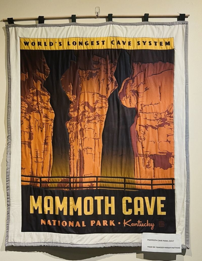 A quilted wall hanging features a vintage-style poster for Mammoth Cave National Park in Kentucky, showing illuminated cave columns and the caption World’s Longest Cave System above the cave entrance.