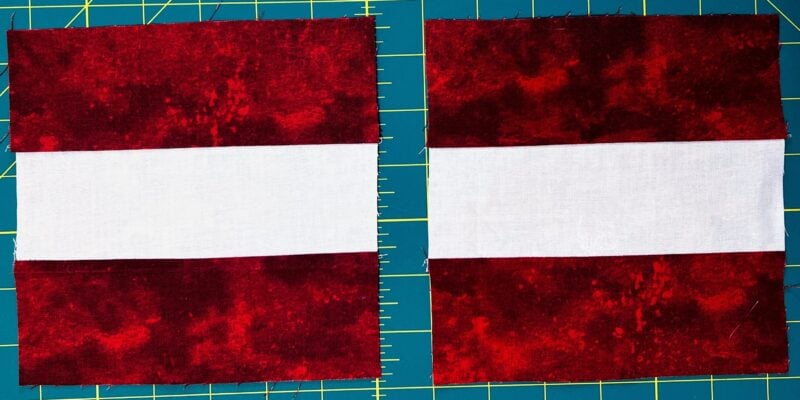 Two quilt blocks each made of three horizontal strips: dark red on the top and bottom, and a white strip in the center. The blocks are placed side by side on a blue cutting mat with a yellow grid.